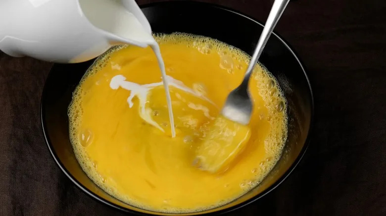 Milk being poured into a bowl of whisked eggs.