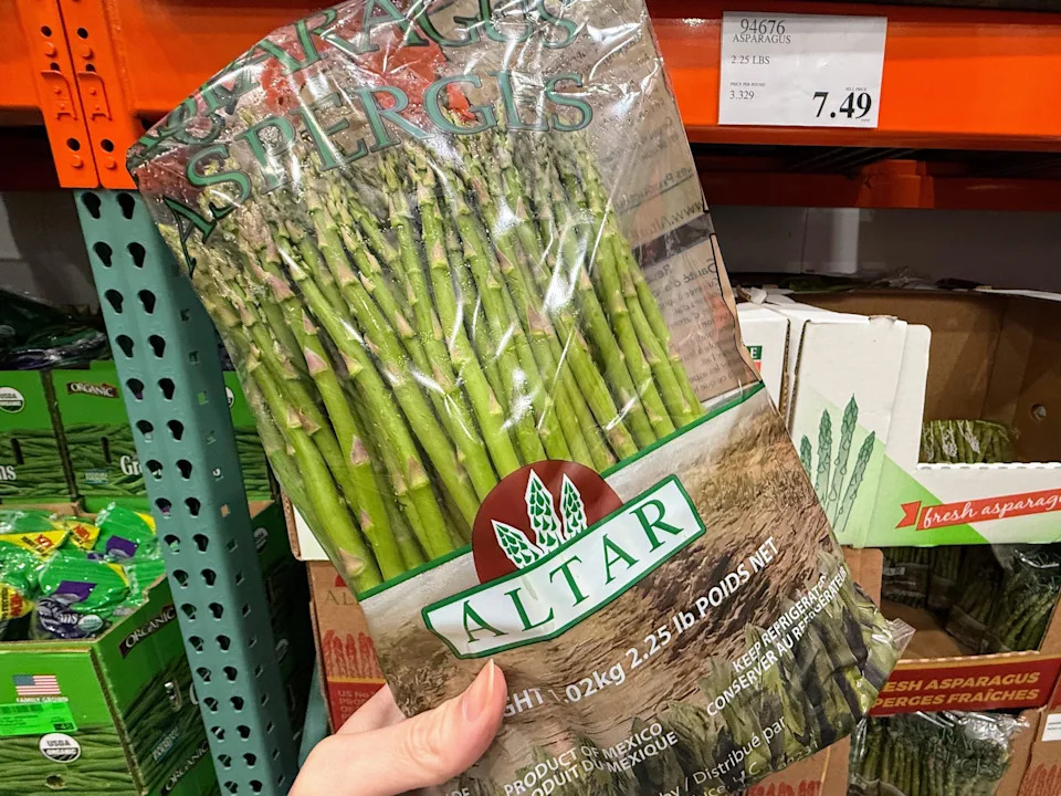 A hand holding a package of asparagus in front of a display at Costco.