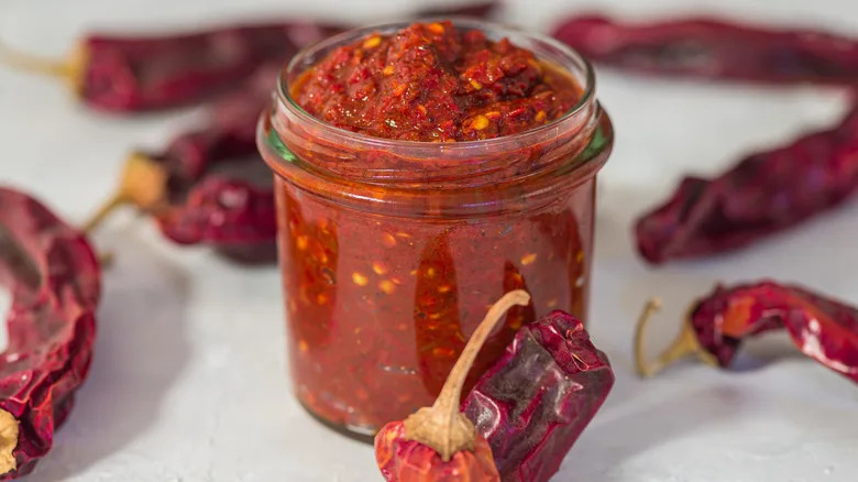 Glass jar of harissa sauce with dried chiles on the side