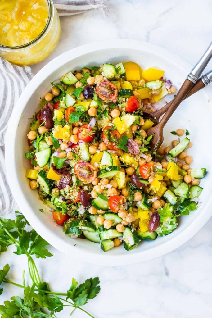 quinoa chickpea salad with tomatoes, olives, cucumbers, pepper, onion, and herbs.
