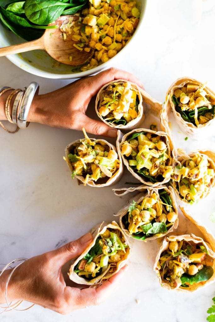 hands holding a bunch of curry chickpea salad wraps.