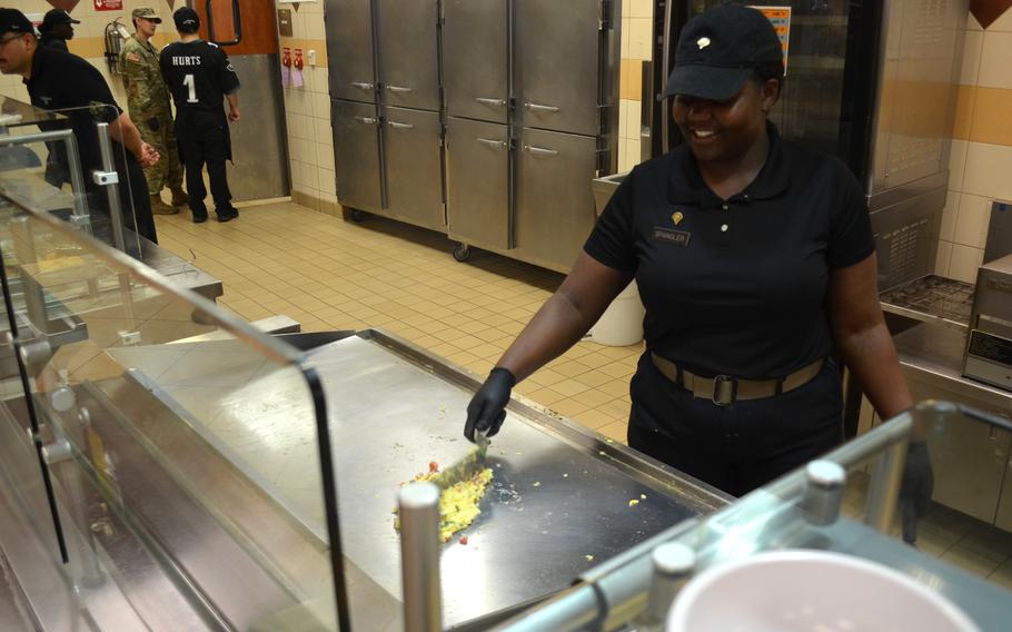 A woman in a blue uniform and hat uses a spatula to cook an omelet on a large flattop grill in a kitchen.