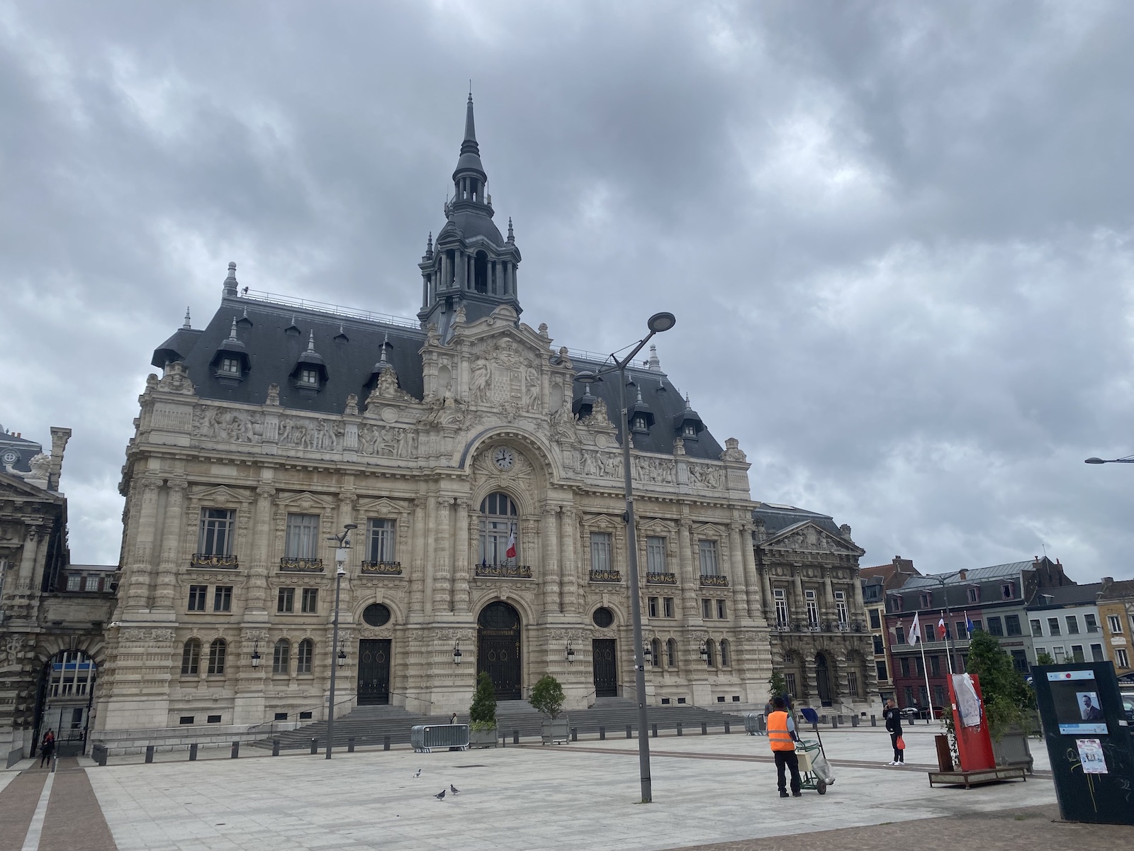 A large stone building with a large square and peoptle in front