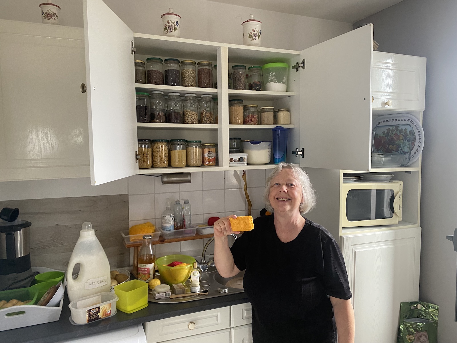 A woman stands in front of an open cupboard filled with dry goods