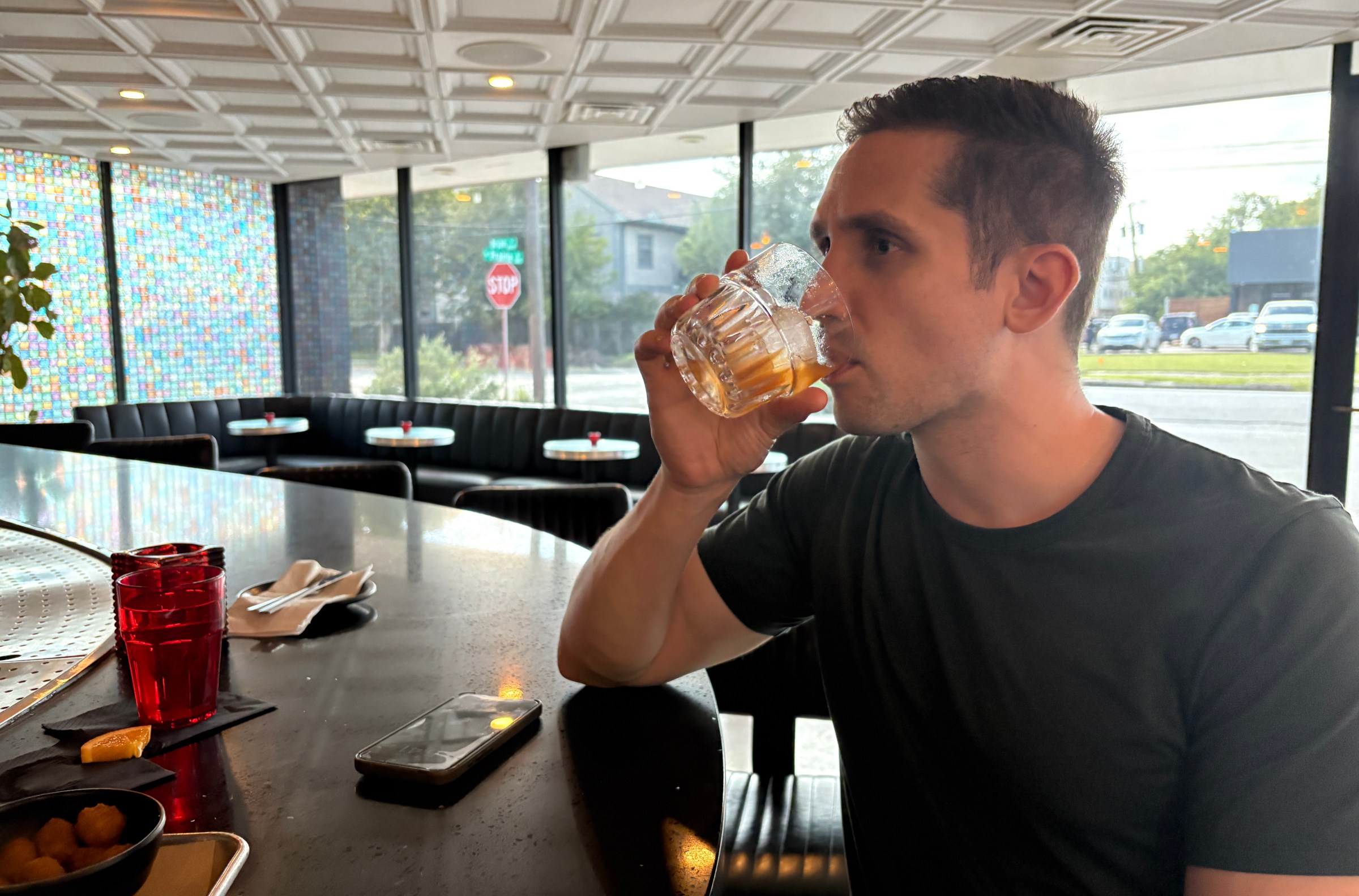 A man sits in a bar, drinking the rest of a nearly empty cocktail.