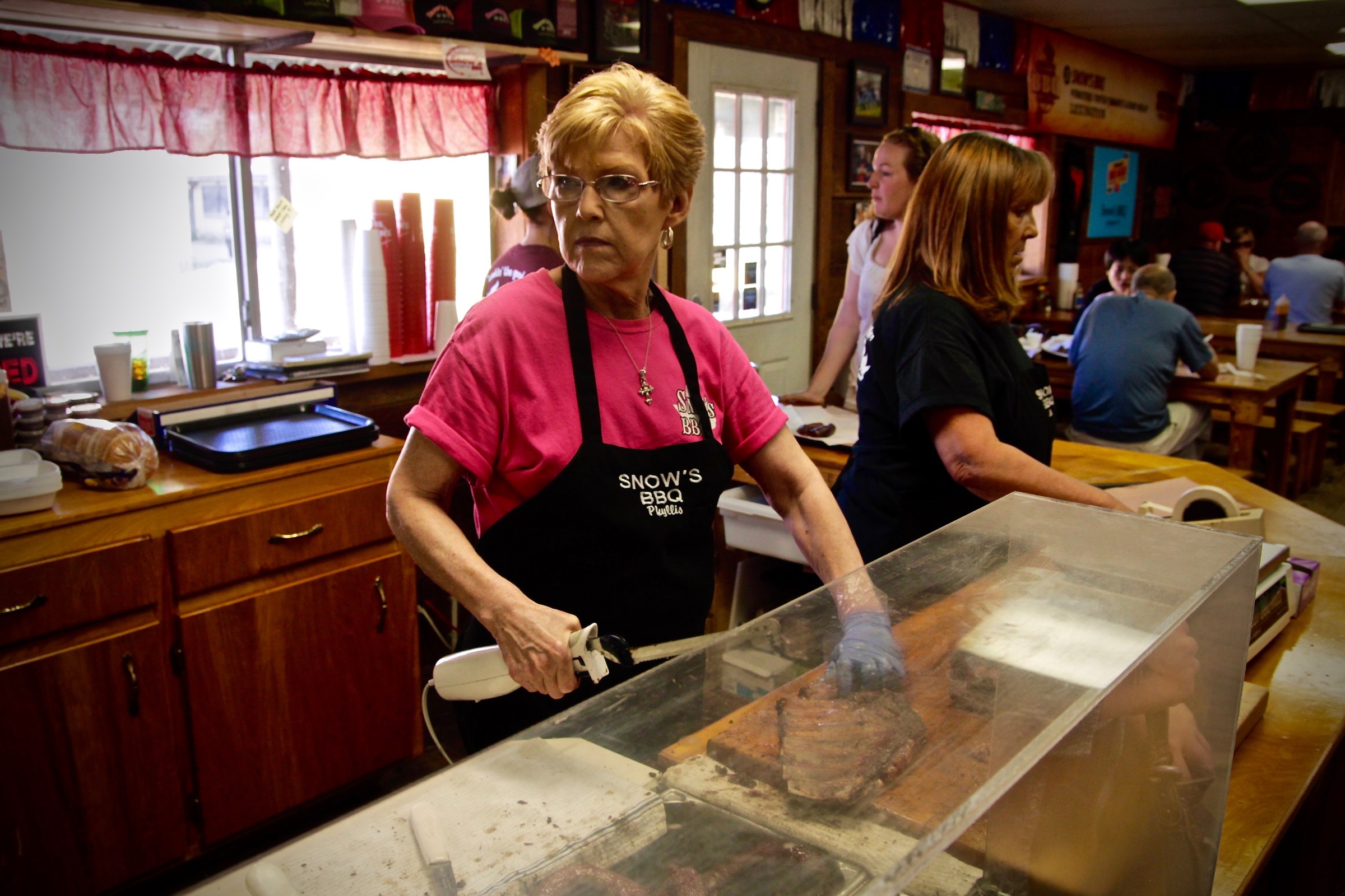 A woman slices through meat with an automatic knife at a barbecue place called Snow’s in Texas.