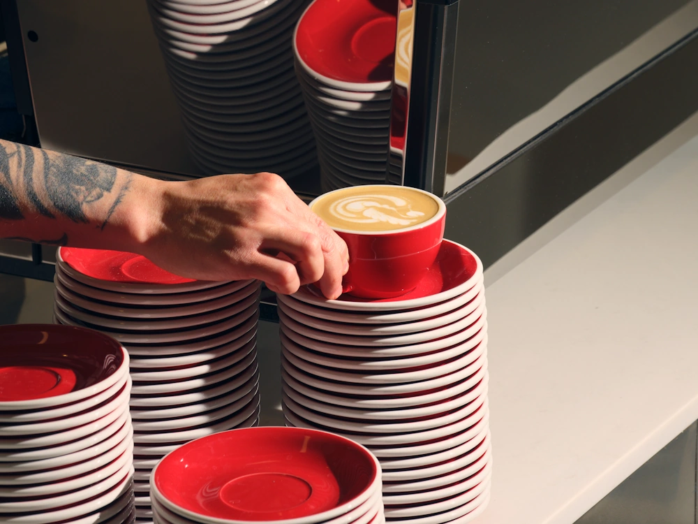 A barista places a milk-based drink on top of a stack of saucers.