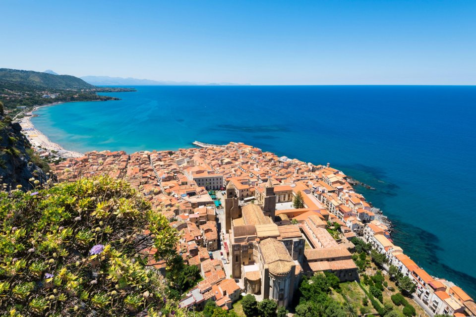 Aerial view of Cefalù, Sicily, showing the town, beach, and sea.