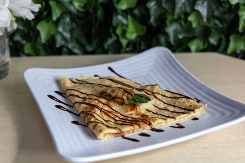 An authentic French crêpe folded and garnished with mushrooms and a mint leaf, drizzled with chocolate sauce, served on a white square plate—a delightful taste of Nashville.