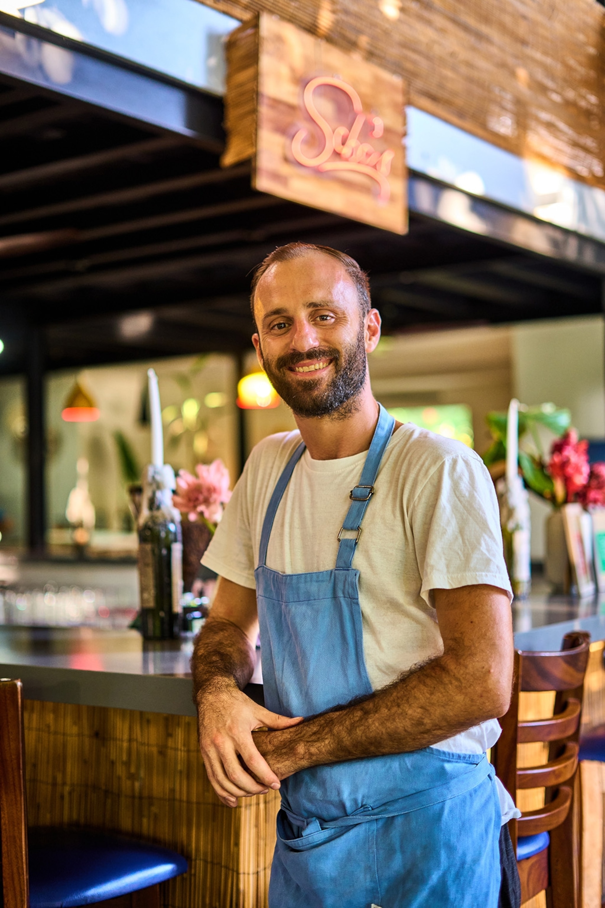 A relaxed chef smiles to camera with a tea towel over his shoulder.