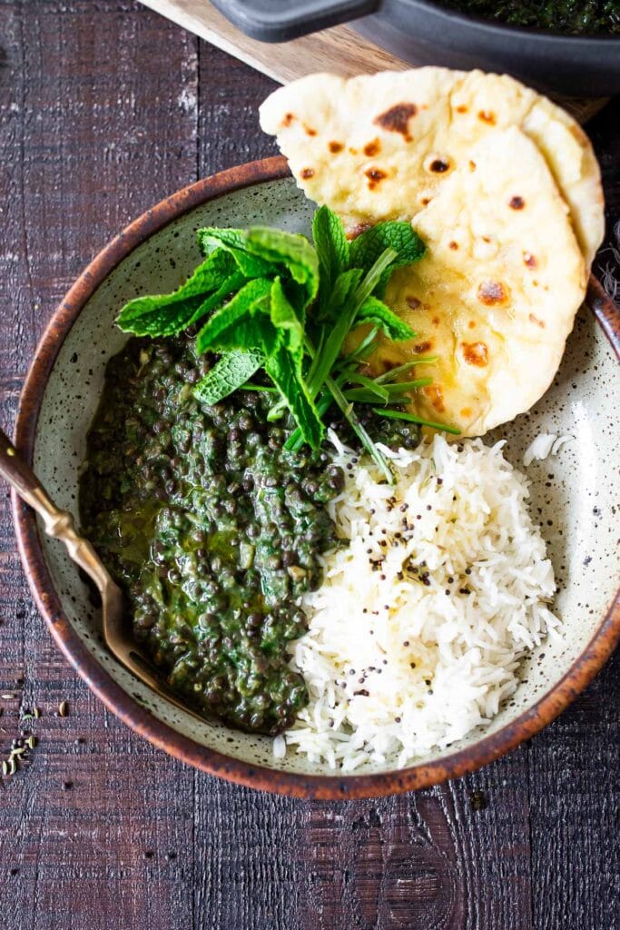 spinach lentil dal served with basmati rice, naan, and fresh herbs.