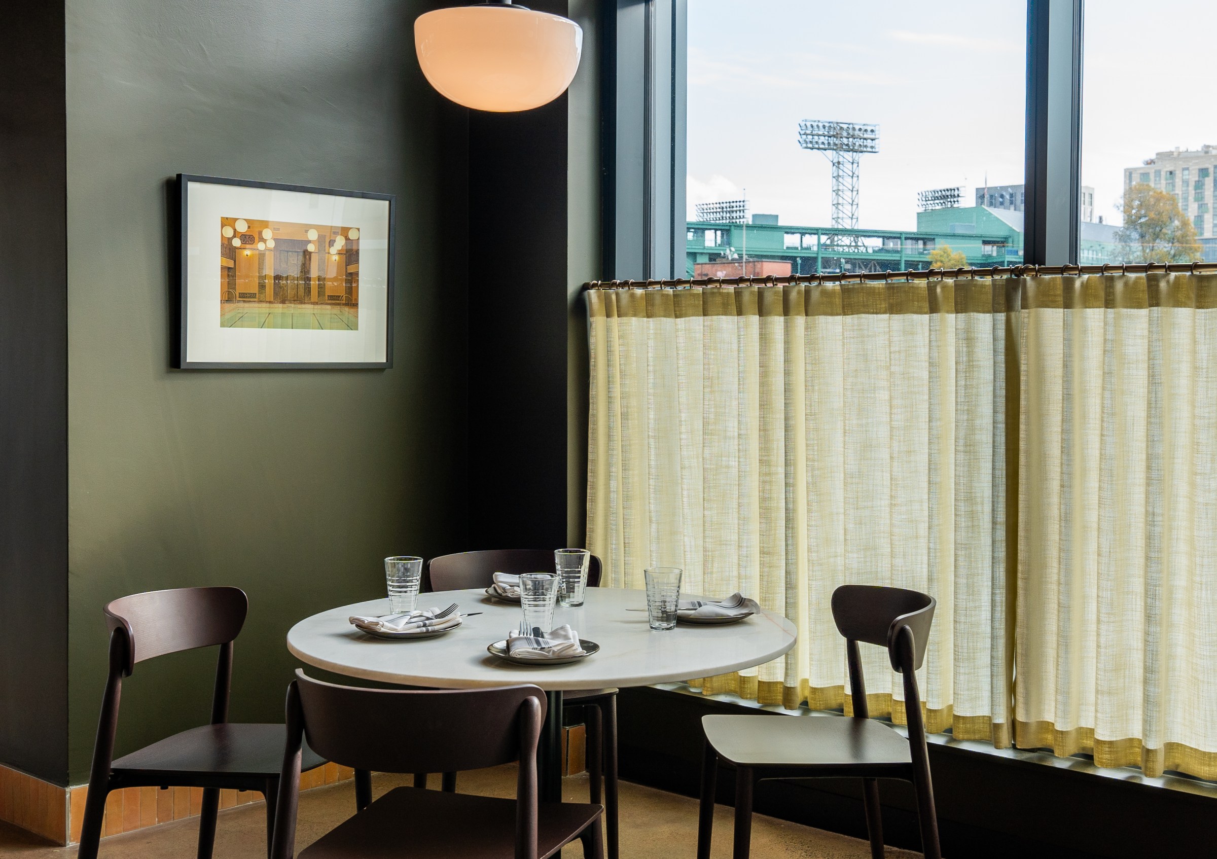 A dining table in the corner of a room with beige half curtains visible over the window.