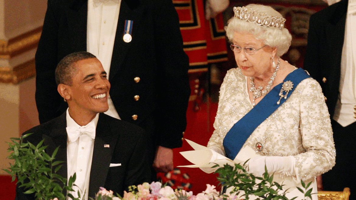 Queen Elizabeth wearing a tiara giving a speech standing up at a banquet table next to Barack Obama