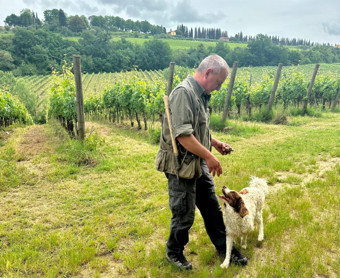 Image of a man and his dog with a beautiful vineyard as a backdrop. The man is a tartufaio, or a truffle hunter, and his companion helps him sniff out truffles.