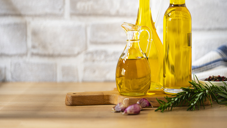 Three bottles of olive oil on a wooden table with garlic and rosemary