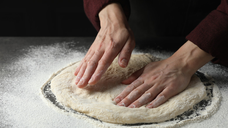 Person stretching pizza dough with hands