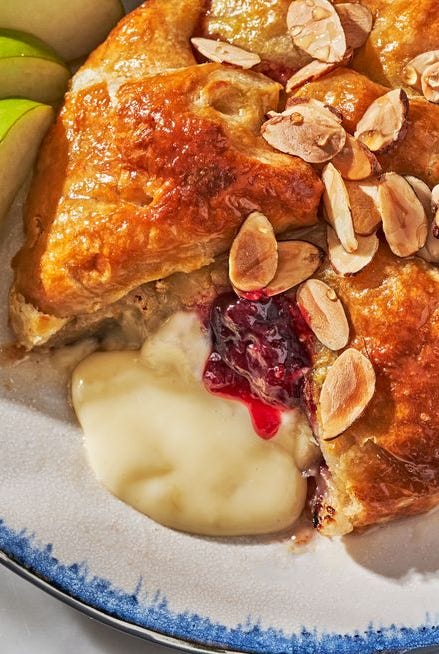 baked brie wrapped with jam in puff pastry on a plate surrounded by fruit and crackers