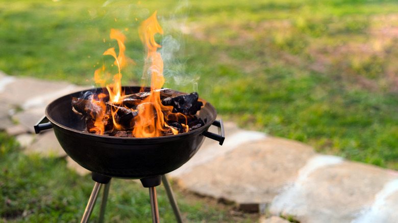 weber style bbq with large flames against the background of a path in a garden