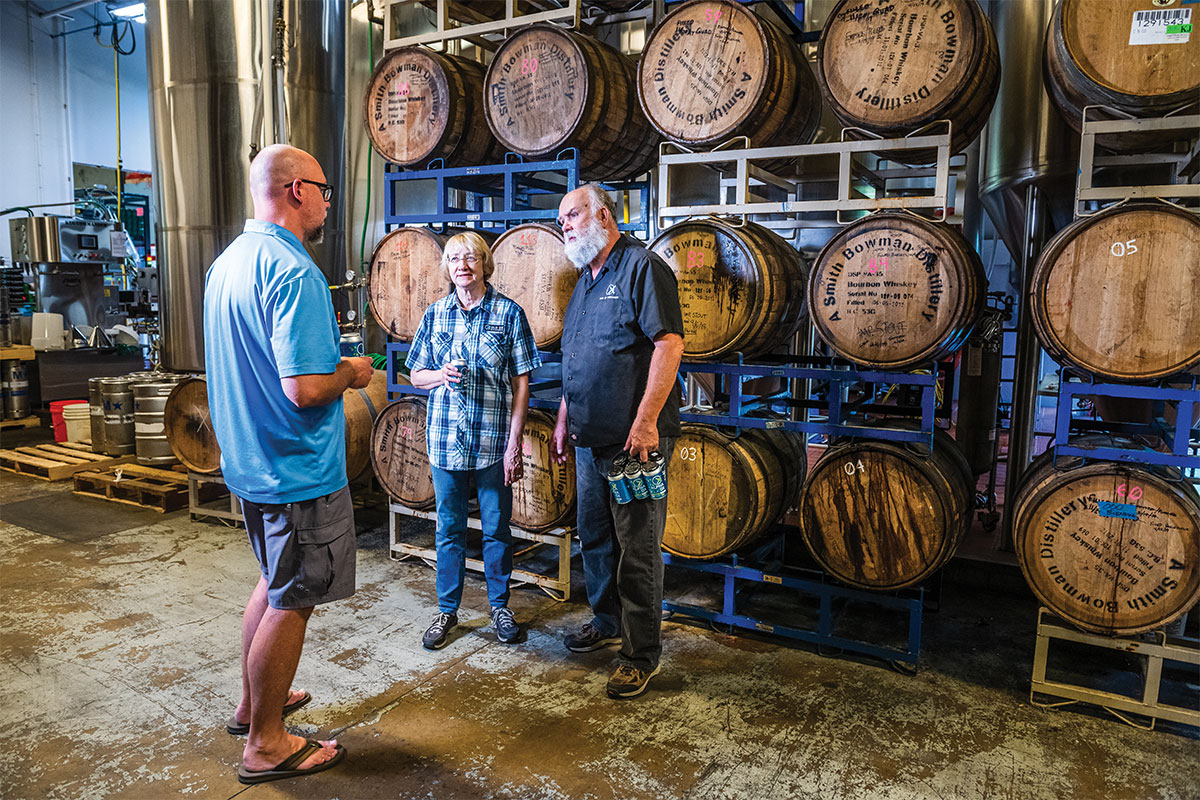 three men talking in front of beer barrels