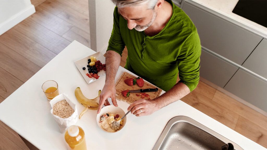 An older adult male prepares a healthy breakfast with oats and fruits on a kitchen countertop
