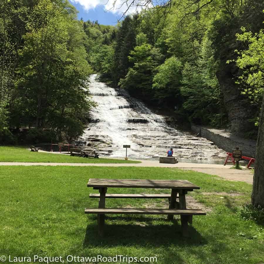wooden picnic table on green grass with waterfall in background