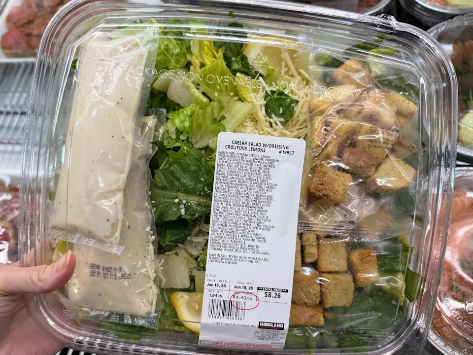 A hand holding a container of Caesar salad at Costco.