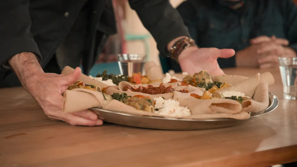 An injera platter being placed on the table by host Stanley Tucci
