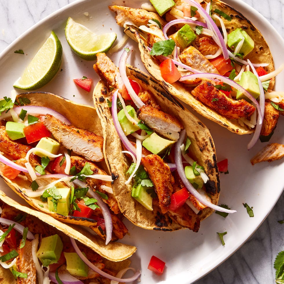 flour tortillas on a plate filled with chicken, tomatoes, avocado and red onion