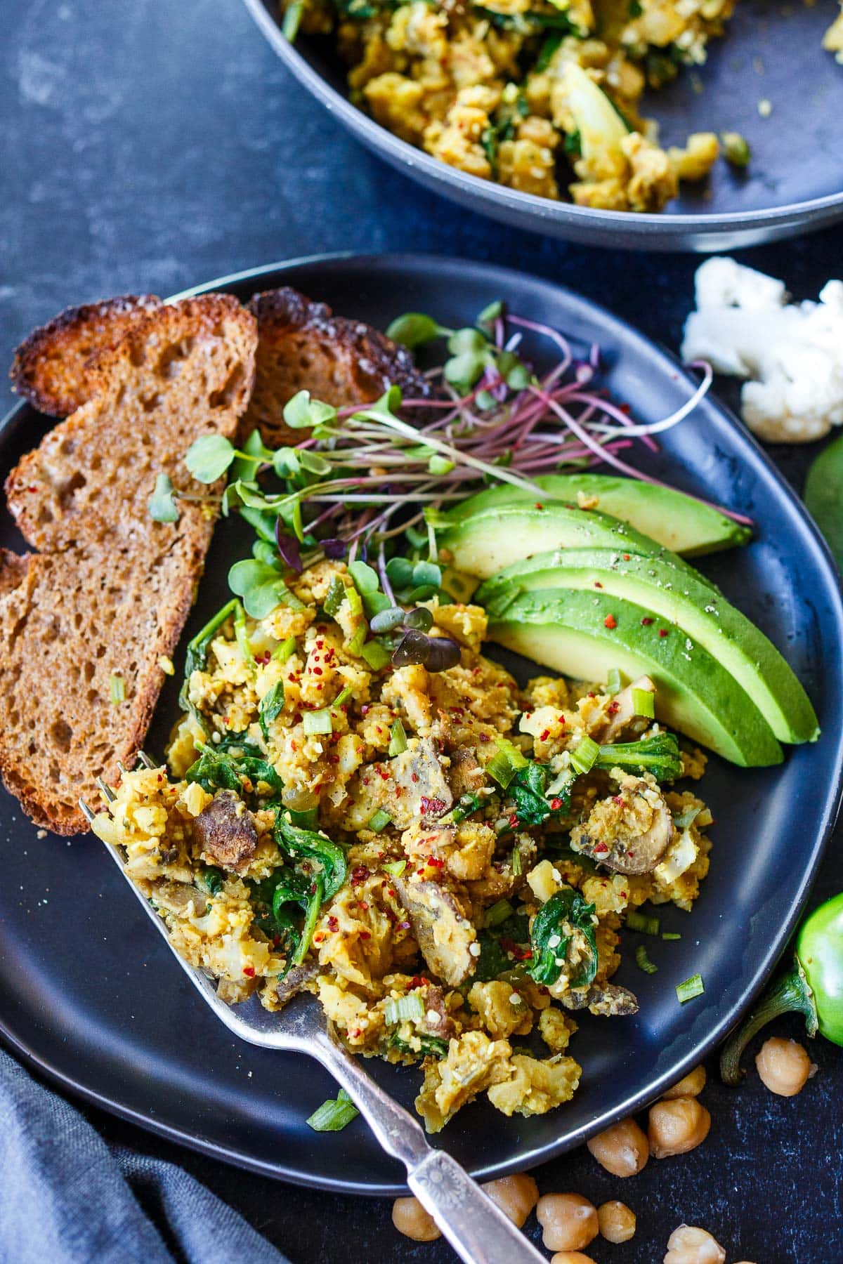chickpea scramble with spinach and mushrooms served with toast, sliced avocado, and micro greens. 