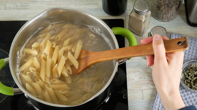 Person stirring and cooking dried pasta
