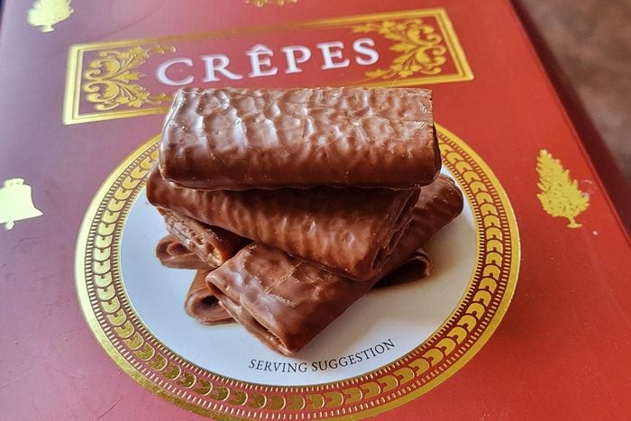A stack of rectangular chocolate-covered crepe cookies sit on top of a red box with a white circle