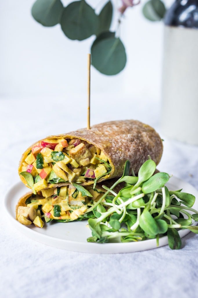 curry tofu wraps with apples, onion, cashews, and herbs stacked with a toothpick, served with sprouts.