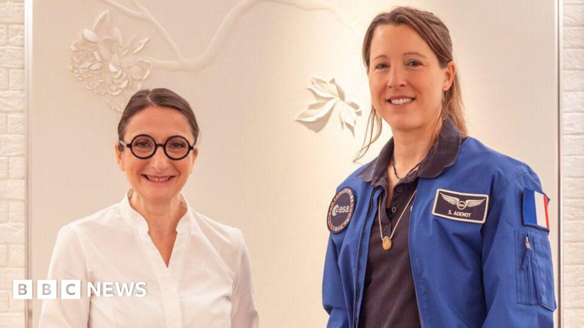 Michelin-starred chef’s lobster bisque and foie gras heading to space Anne-Sophie Pic, wearing a white shirt and her signature black round glasses, and Sophie Adenot, wearing a blue Nasa jacket, stand together smiling.