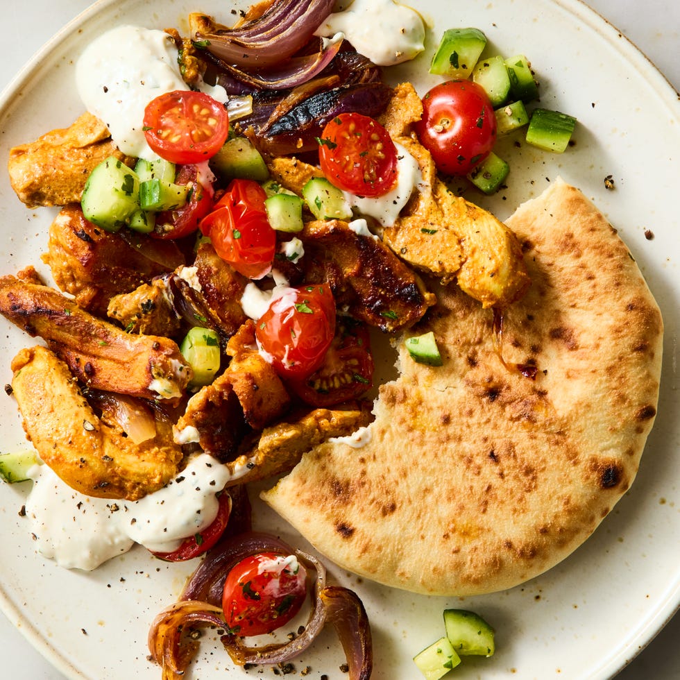 strips of chicken thigh are marinated in greek yogurt, cumin, coriander, and paprika, roasted on a sheet pan with red onion, then topped with a bright cucumber tomato salad and herby tahini yogurt dressing