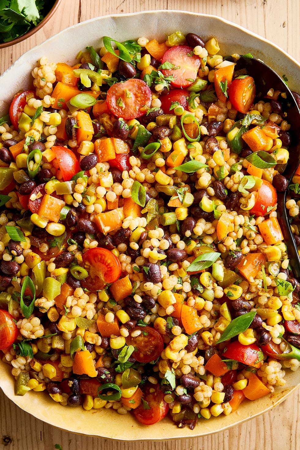a bowl with pearl couscous, black beans, corn, bell peppers, cherry tomatoes, scallions, cilantro, and pickled jalapenos