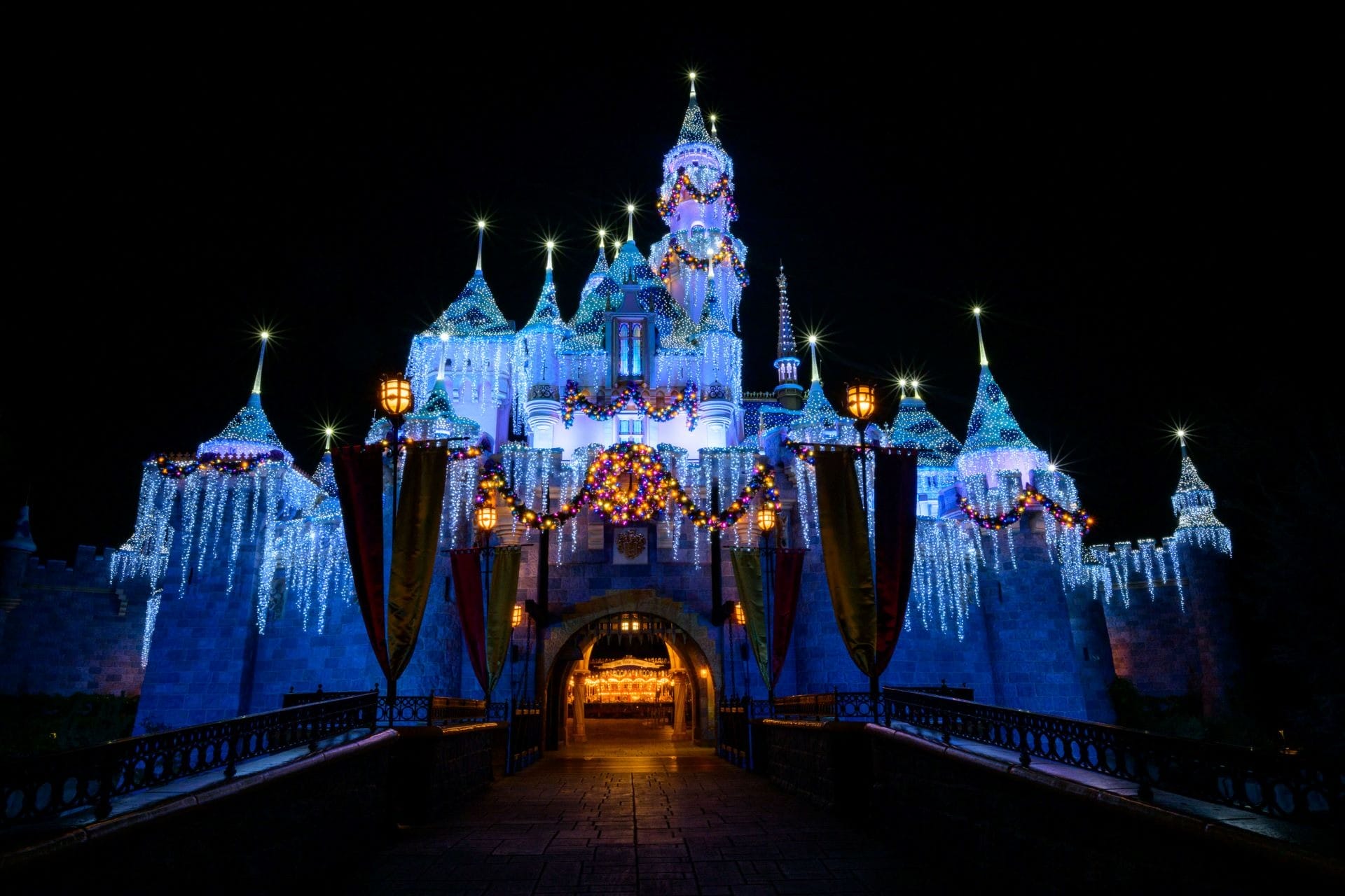Sleeping Beauty Castle in Disneyland Park at night, decorated with holiday garlands and icecicle lights.