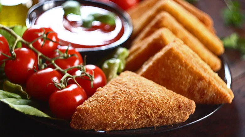 A traditional mozzarella en carrozza, quartered and deep-fried into triangles, served with cherry tomatoes and sauce