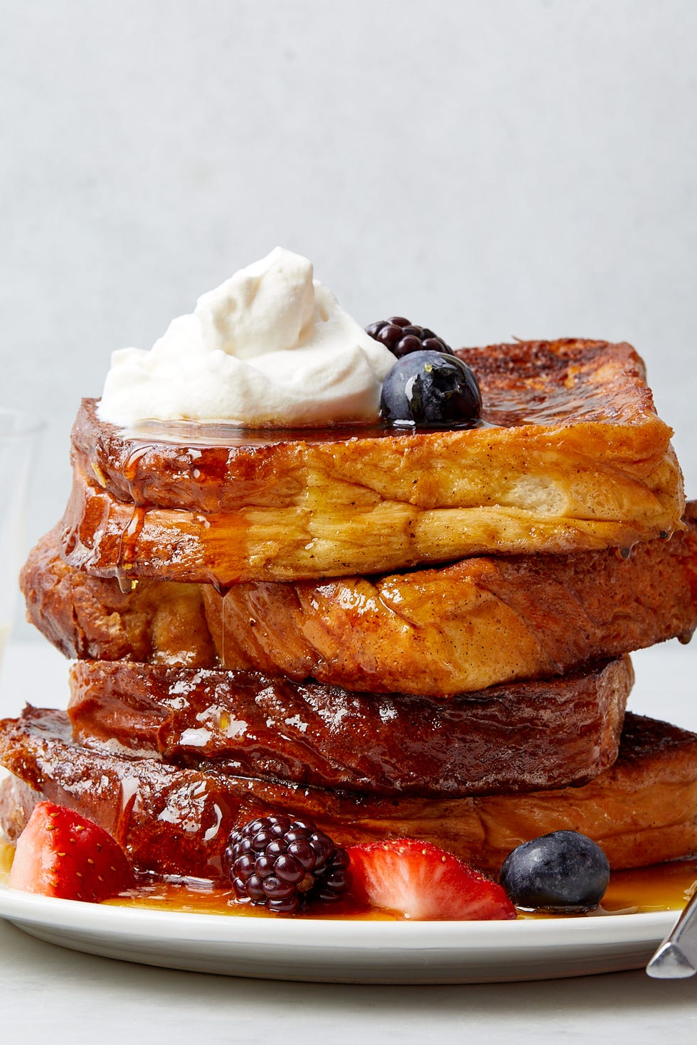 eggnog french toast topped with whipped cream and berries on a plate with a glass and jug of eggnog in the background