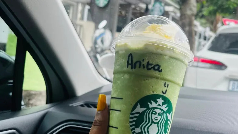 a hand with orange nails holding a Matcha-Misu drink in a car