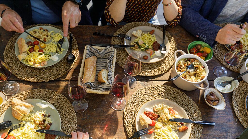 A group of people having dinner, with their four plates full of Mediterranean foods, as glasses of red wine accompany their meal