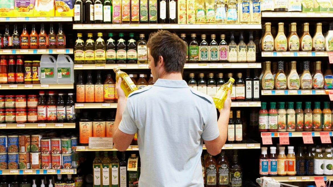 man holding bottles of oil in supermarket aisle