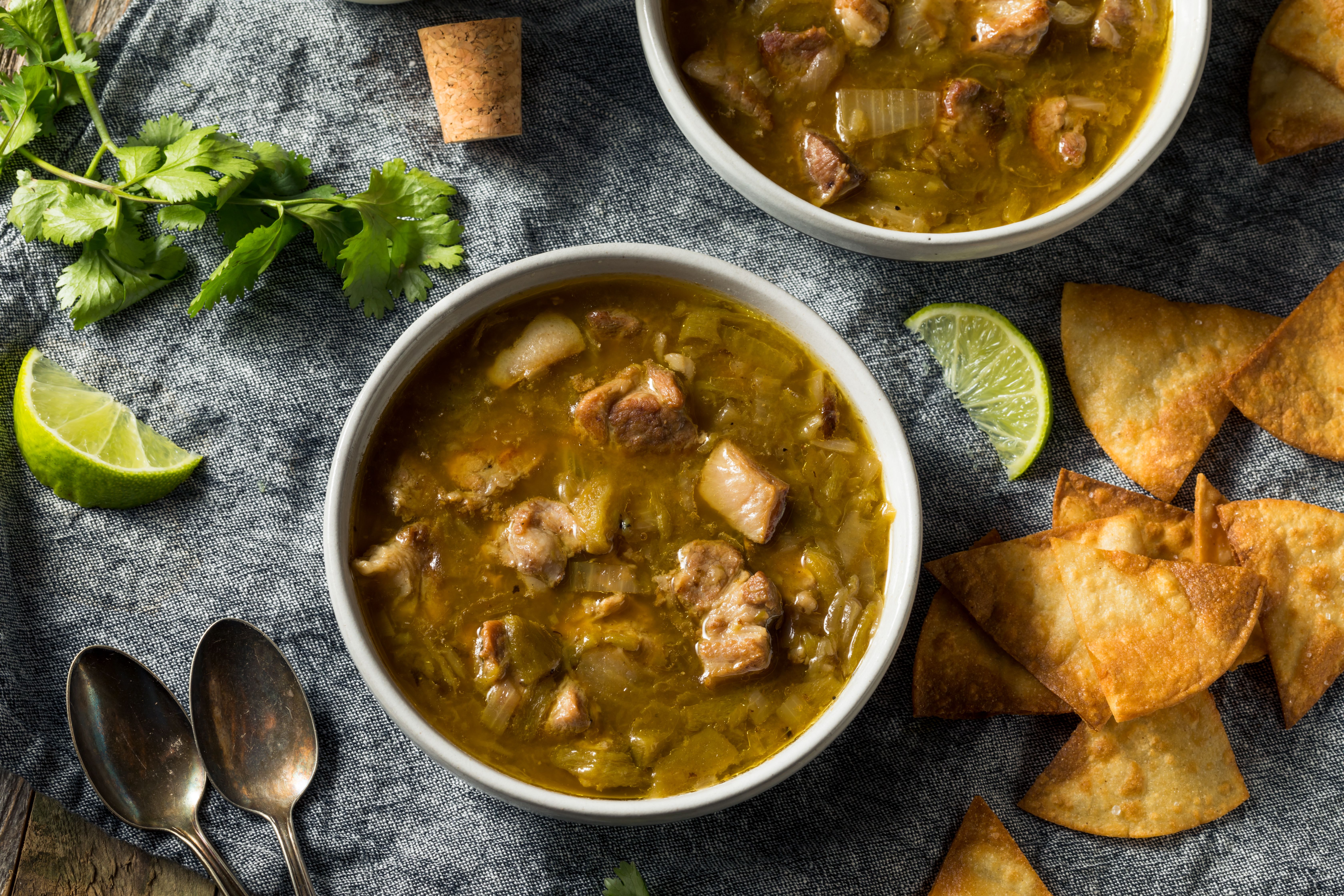 A bowl of green chili with tortilla chips and spoons on the table