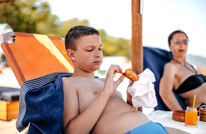 photo of Parent spending time together with teenager son on vacation on the beach eating