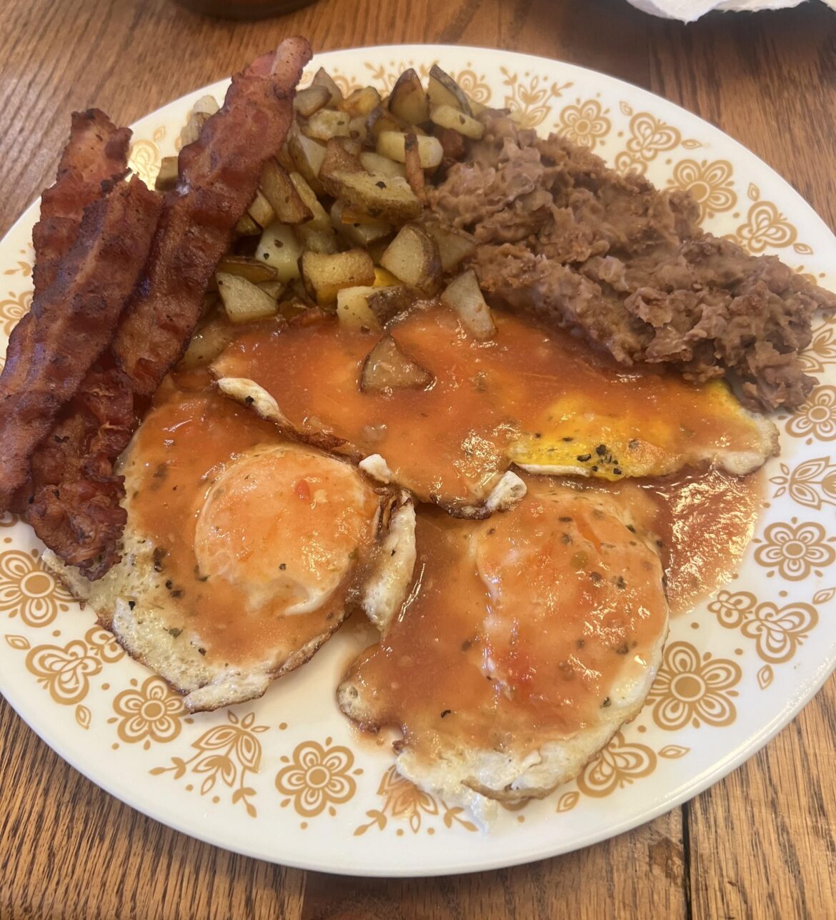 Desayunos huevos con salsa roja, tocino, patatas y frijoles refritos.