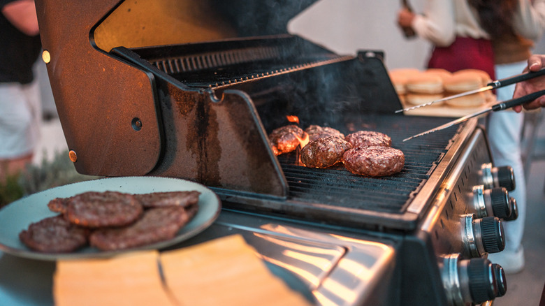 Hamburger patties on the grill with cheese outside.