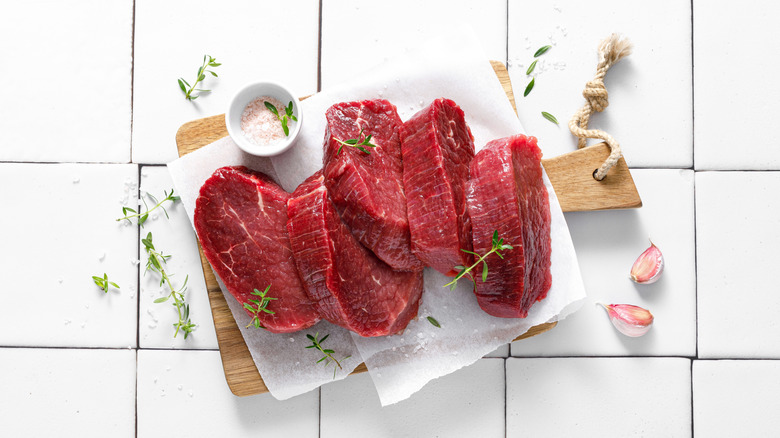 A stack of raw steaks surrounded by salt, garlic and herbs