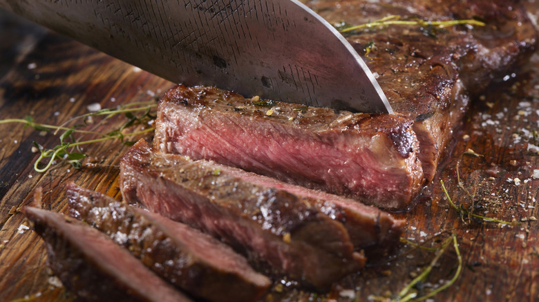 Medium rare grilled strip steak with thyme, knife, board