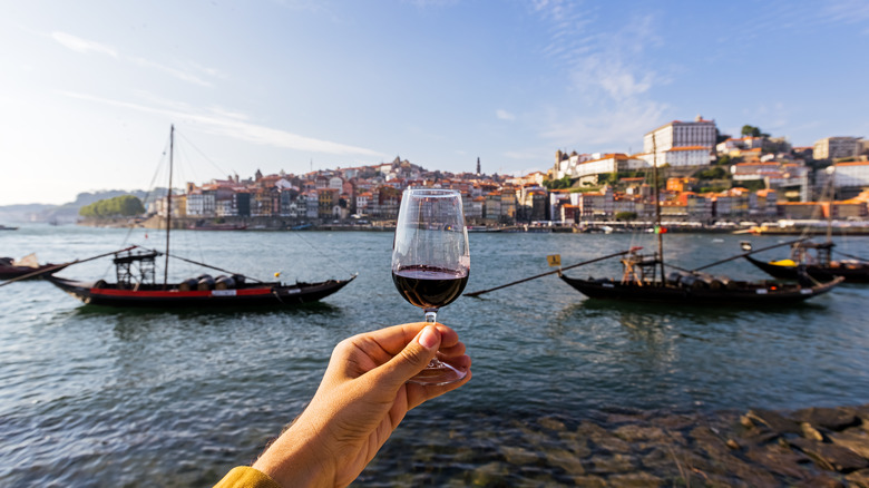 woman holds glass of ruby port wine in front of porto
