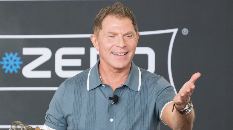 An animated Bobby Flay smiles as he reaches out to his audience, likely mid-conversation about food