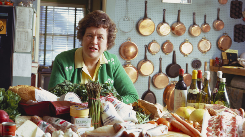 A smiling Julia Child, sitting down with a couple of glasses in front of her -- some filled with water, some with wine